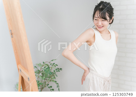 微笑的亞洲女人在鏡子裡檢查她的臀部（臀部向上） 125303749
