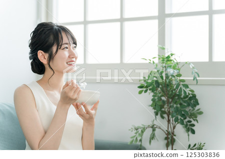 Asian women eating yogurt and dairy products on the sofa at home (bifidobacterium, lactic acid bacteria, dairy products, intestinal activity) 125303836