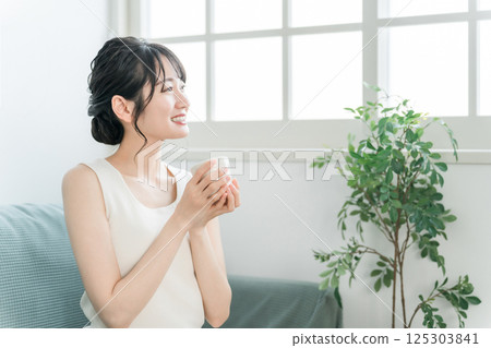 一位輕鬆的亞洲女性,早上在家用杯子喝茶和熱水(Onkatsu) 一位輕鬆的亞洲女性,早上在家用杯子喝茶和熱水(Onkatsu) 125303841