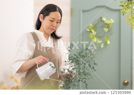 Smiling adult woman taking care of plants indoors | Healthy living image | Well-being girl | Well-being 125303990