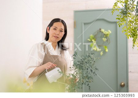 Smiling adult woman taking care of plants indoors | Healthy living image | Well-being girl | Well-being 125303993
