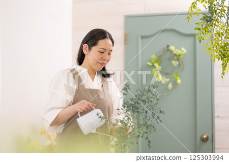 Smiling adult woman taking care of plants indoors | Healthy living image | Well-being girl | Well-being 125303994