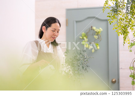 Smiling adult woman taking care of plants indoors | Healthy living image | Well-being girl | Well-being Smiling adult woman taking care of plants indoors | Healthy living image | Well-being girl | Well-being 125303995