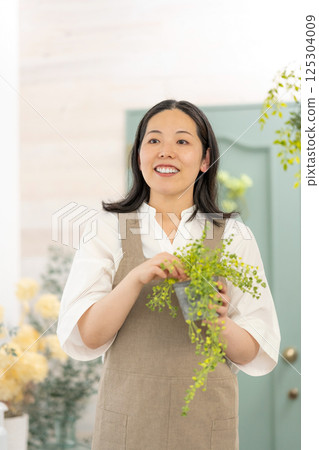 Smiling adult woman taking care of plants indoors | Healthy living image | Well-being girl | Well-being 125304009