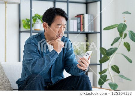 Middle-aged man using a smartphone in the living room Middle-aged man using a smartphone in the living room 125304132