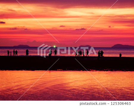 silhouettes sunset, people on the beach at sunset, group of people gathered on a beach at sunset, looking out at the vibrant pink and orange sky and the ocean with distant islands, ocean sunset 125306463
