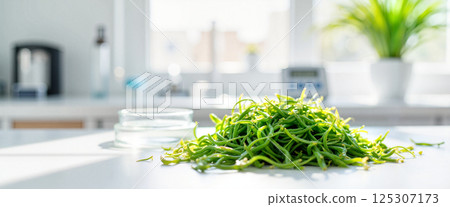 Fresh green vegetable pile sits on a table, surrounded by bright natural light from windows in a modern kitchen. A glass dish is nearby, and a potted plant is visible in the background 125307173