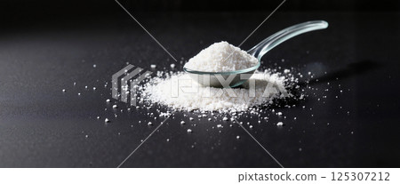 Fine white granules in a spoon on a dark surface, with some particles scattered around, conveying a sense of precision and simplicity in presentation Fine white granules in a spoon on a dark surface, with some particles scattered around, conveying a sense of precision and simplicity in presentation 125307212