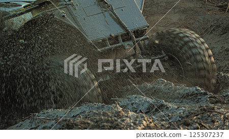 Close-up of the front end of an SUV that got stuck in the mud. The wheels are spinning, splashes and mud are flying from under them. Extreme mud racing Close-up of the front end of an SUV that got stuck in the mud. The wheels are spinning, splashes and mud are flying from under them. Extreme mud racing 125307237
