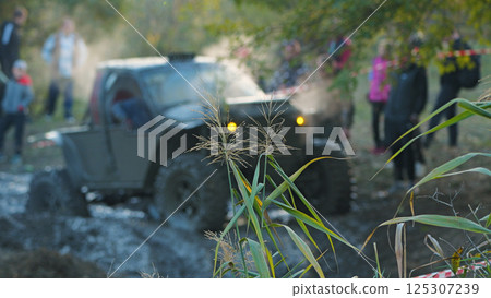 On the background of green grass dirty SUV in the mud. Extreme races in the mud. Off-road vehicle racing through a muddy course with spectators watching On the background of green grass dirty SUV in the mud. Extreme races in the mud. Off-road vehicle racing through a muddy course with spectators watching 125307239