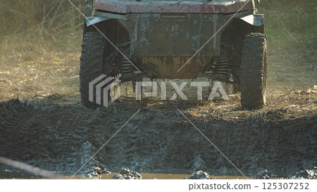 A close-up of an off-road vehicle with large, muddy tires navigating a challenging terrain. The suspension system is visible, suggesting the vehicle is built for rough conditions A close-up of an off-road vehicle with large, muddy tires navigating a challenging terrain. The suspension system is visible, suggesting the vehicle is built for rough conditions 125307252