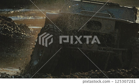 A close-up of a muddy, powerful off-road vehicle driving through a muddy puddle, creating a cloud of spray. Epic moment of extreme off-road competitions A close-up of a muddy, powerful off-road vehicle driving through a muddy puddle, creating a cloud of spray. Epic moment of extreme off-road competitions 125307281