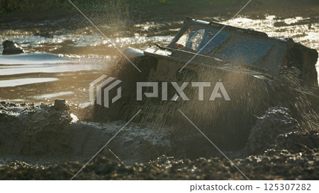 Dirty powerful SUV stuck in a muddy puddle, spraying water and mud high into the air. Epic moment of extreme off-road competitions Dirty powerful SUV stuck in a muddy puddle, spraying water and mud high into the air. Epic moment of extreme off-road competitions 125307282