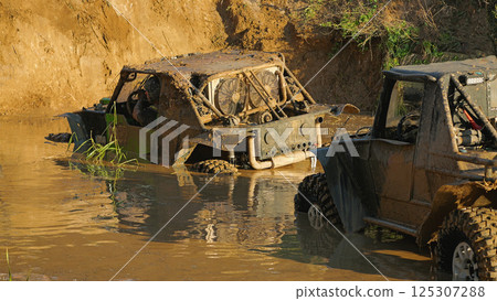 Two SUVs are standing in a muddy ditch. In front of them is a steep dirt wall. Extreme racing on off-road vehicles Two SUVs are standing in a muddy ditch. In front of them is a steep dirt wall. Extreme racing on off-road vehicles 125307288