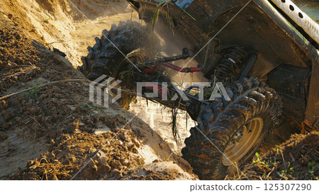 Close-up of the front of an off-road vehicle stuck in a muddy ditch. The vehicle is partially submerged in mud. Large wheels and suspension elements are clearly visible Close-up of the front of an off-road vehicle stuck in a muddy ditch. The vehicle is partially submerged in mud. Large wheels and suspension elements are clearly visible 125307290
