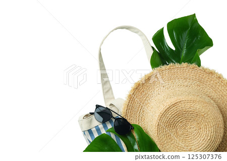 Stylish beach hat, sunglasses, and tote surrounded by tropical leaves, isolated on white background 125307376
