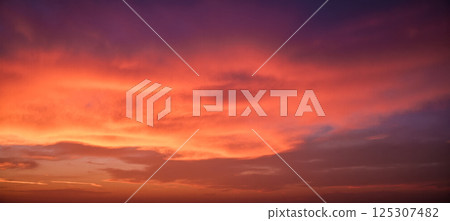 Peaceful evening sky in shades of red orange and violet with glowing clouds at sunset over quiet horizon, dreamy soft background for themes 125307482