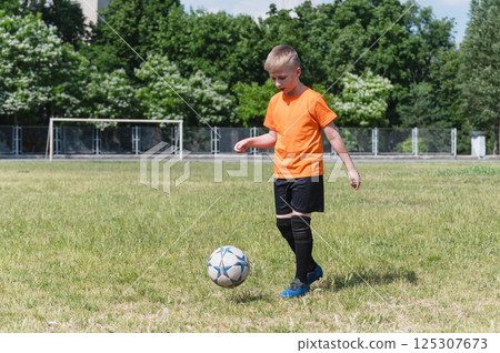 Boy kicking soccer ball on sunny grassy field. Boy kicking soccer ball on sunny grassy field. 125307673