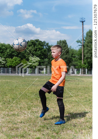 Boy juggling soccer ball on grassy field in sunlight. 125307679