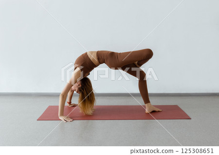 An attractive girl sits on a yoga mat. Slim body and health care. Urdhva Dhanurasana , Inverted Bow Pose or Bridge Pose 125308651