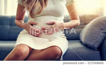 Close-up of a pregnant woman sitting on a sofa and rubbing her belly in a relaxed manner 125308688
