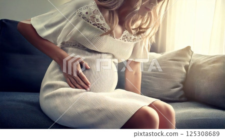 A pregnant woman sitting on a sofa, leaning forward and rubbing her stomach in pain, labor pains, abdominal pain 125308689