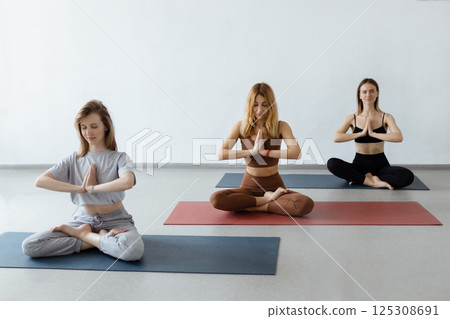 Group athletic attractive girls sit in lotus position on yoga mat indoors .Yoga, fitness and healthy lifestyle 125308691