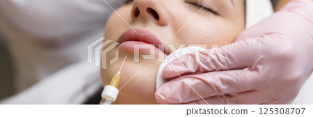 lip shape correction procedure in a cosmetology salon. The specialist makes an injection on the lips of the patient. Lip augmentation. lip shape correction procedure in a cosmetology salon. The specialist makes an injection on the lips of the patient. Lip augmentation. 125308707