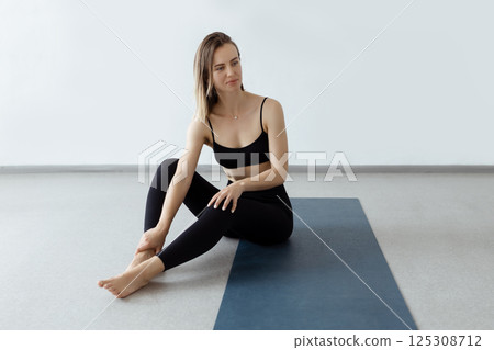 An attractive girl sits on a yoga mat. Slim body and health care An attractive girl sits on a yoga mat. Slim body and health care 125308712