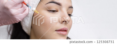 Cosmetologist makes rejuvenating anti wrinkle injections on the face of a beautiful woman. Female aesthetic cosmetology in a beauty salon. Cosmetologist makes rejuvenating anti wrinkle injections on the face of a beautiful woman. Female aesthetic cosmetology in a beauty salon. 125308731