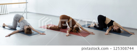 Group of young sporty people practicing yoga lesson with instructor, stretching in Child exercise, Balasana pose, working out, indoor close up, students training in club, studio Group of young sporty people practicing yoga lesson with instructor, stretching in Child exercise, Balasana pose, working out, indoor close up, students training in club, studio 125308744