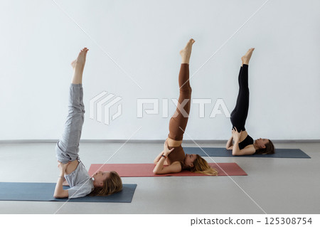 Young women standing in pose with legs up during yoga workout. Young women standing in pose with legs up during yoga workout. 125308754