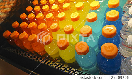 Colorful plastic bottles of sports drinks are displayed in a rainbow-like gradation on the store's refrigerated shelves. 125309206