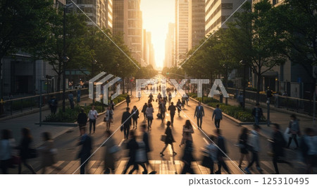 Warm rays of sunlight illuminate a busy city street as pedestrians move across the intersection during the golden hour. Skyscrapers line the street, their reflections shimmering in the evening glow 125310495