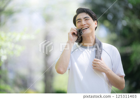 Close-up of a refreshing young man wiping sweat from running sports or exercise in the fresh greenery under blue sky 125311403