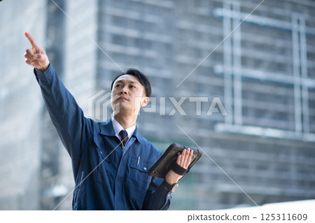 A man operating a tablet device at a large construction site A man operating a tablet device at a large construction site 125311609