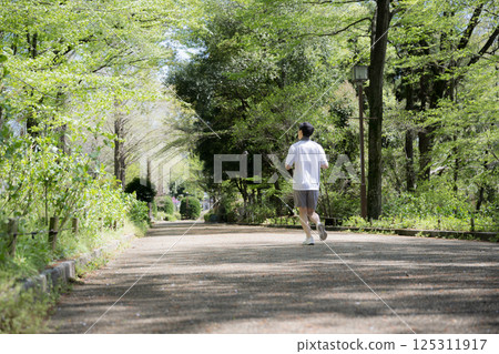 Full-body wide-angle shot of a man running or jogging under the fresh greenery of the blue sky. Refreshing exercise, sporty image. No face. Full-body wide-angle shot of a man running or jogging under the fresh greenery of the blue sky. Refreshing exercise, sporty image. No face. 125311917
