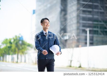 A male contractor walking in front of a large construction site 125312414