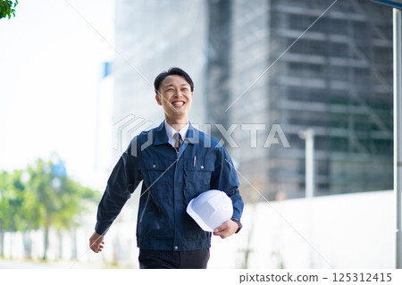 A male contractor walking in front of a large construction site 125312415