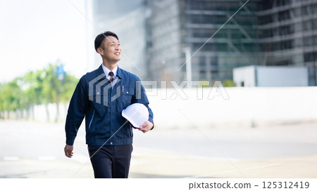 A male contractor walking in front of a large construction site A male contractor walking in front of a large construction site 125312419