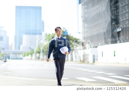A male contractor walking in front of a large construction site A male contractor walking in front of a large construction site 125312420