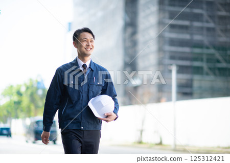 A male contractor walking in front of a large construction site A male contractor walking in front of a large construction site 125312421