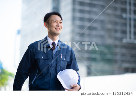 A male contractor walking in front of a large construction site A male contractor walking in front of a large construction site 125312424