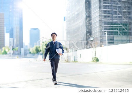 A male contractor walking in front of a large construction site 125312425