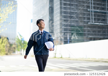 A male contractor walking in front of a large construction site A male contractor walking in front of a large construction site 125312426