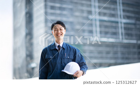 一名男性承包商站在一個大型建築工地前 125312627