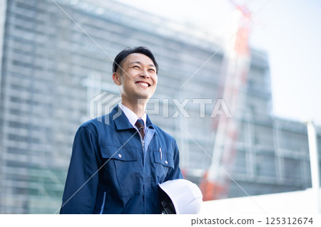 A male contractor walking in front of a large construction site A male contractor walking in front of a large construction site 125312674