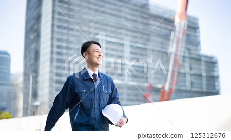 A male contractor walking in front of a large construction site A male contractor walking in front of a large construction site 125312676