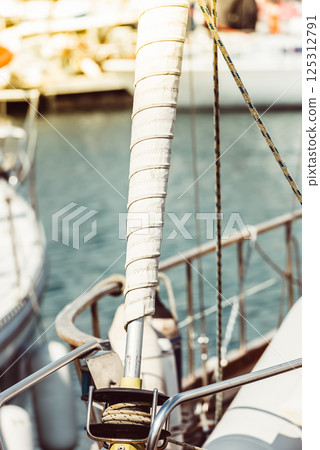 Sailboat mast with wrapped sail detail in marina setting, ideal for nautical background 125312791