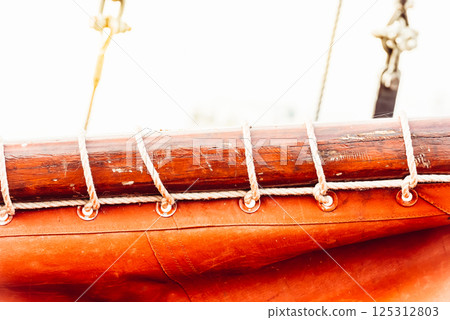 Sailboat mast and ropes with vibrant orange sail creating nautical background Sailboat mast and ropes with vibrant orange sail creating nautical background 125312803